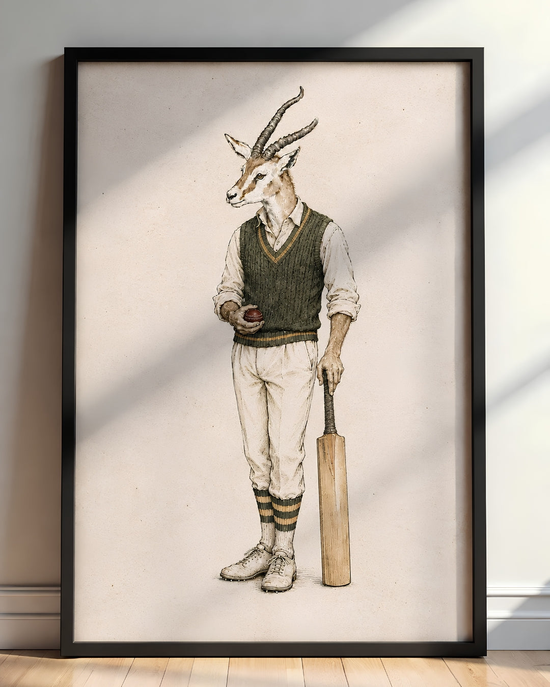 A framed art print featuring a whimsical illustration of a gazelle dressed in vintage cricket attire, holding a bat and ball, leaning against a wall on a wooden floor.