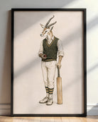 A framed art print featuring a whimsical illustration of a gazelle dressed in vintage cricket attire, holding a bat and ball, leaning against a wall on a wooden floor.