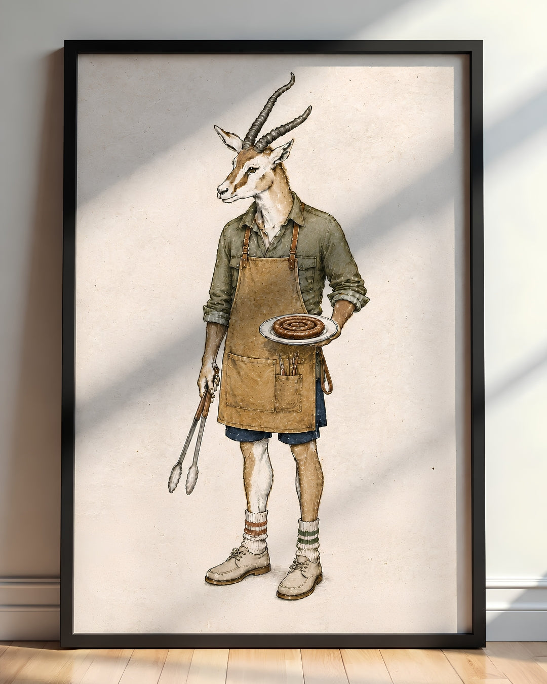 A framed art print featuring a whimsical illustration of a gazelle dressed as a chef, wearing an apron and holding a plate with a burger, standing on a light wood floor against a white wall with soft window shadows.