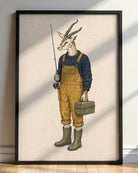 A framed art print featuring a whimsical illustration of a gazelle dressed as a fisherman, standing on a light wood floor against a white wall with soft window shadows.