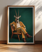 A framed art print leaning against a wall on a wooden floor. The print shows a stylized portrait of a seated person wearing a yellow tracksuit with green stripes, a white shirt, and a giraffe head mask, set against a dark green background.