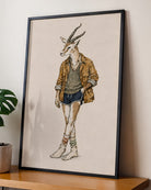 A framed art print featuring a whimsical illustration of a gazelle dressed in casual clothing, leaning against a beige wall on a wooden shelf next to a potted plant.