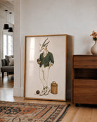 A large framed art print featuring a whimsical illustration of a gazelle dressed in vintage bowling attire, leaning against a white wall in a modern living room setting.