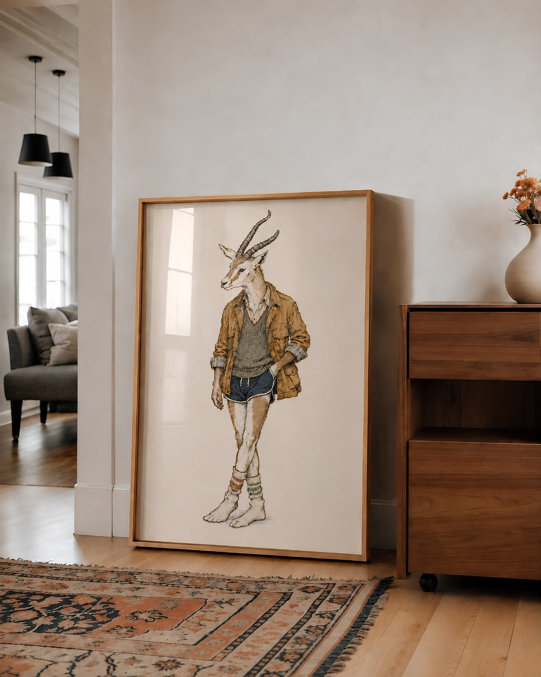A large framed art print featuring a whimsical illustration of a gazelle dressed in casual clothing, leaning against a white wall in a modern living room setting.
