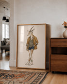 A large framed art print featuring a whimsical illustration of a gazelle dressed in casual clothing, leaning against a white wall in a modern living room setting.