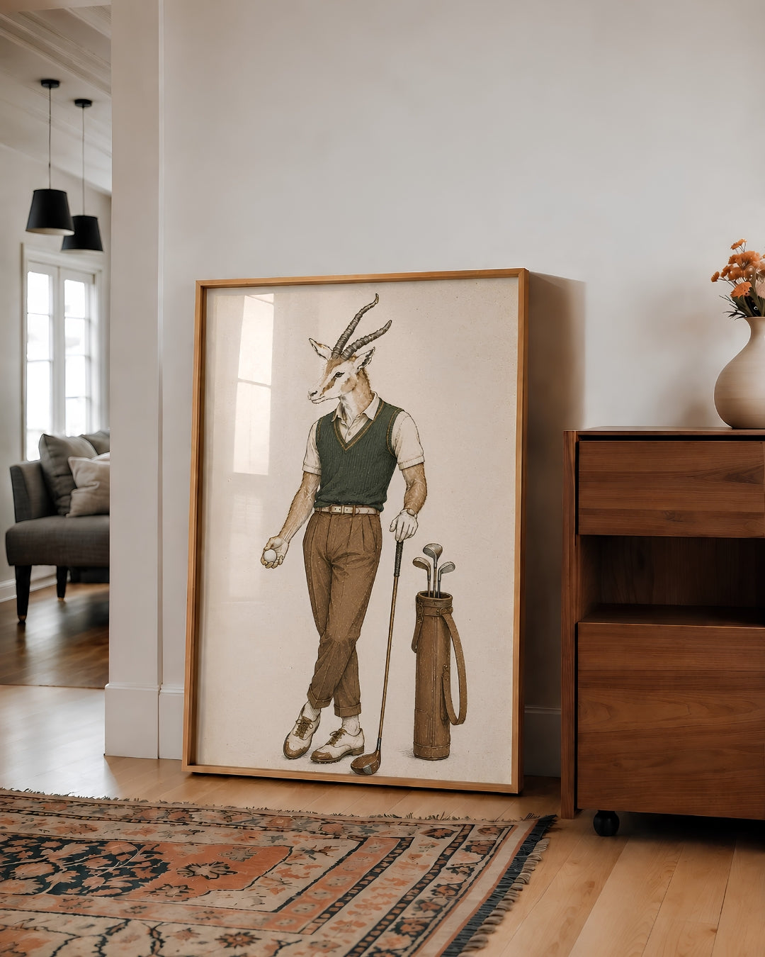 A large framed art print featuring a whimsical illustration of a male antelope dressed in golf attire, leaning against a white wall in a modern living room setting.