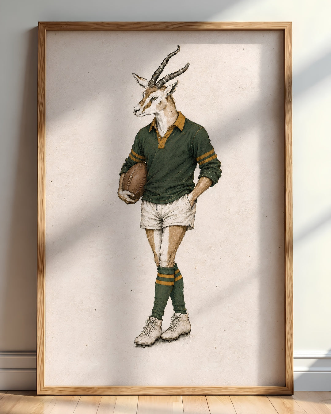 A framed art print featuring a vintage-style illustration of a springbok antelope dressed in a green rugby jersey, white shorts, and green socks, leaning against a wall on a wooden floor.