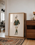 A large framed art print leaning against a white wall in a modern living room. The print features a whimsical illustration of a springbok antelope dressed in a vintage rugby jersey, shorts, socks, and holding a rugby ball.